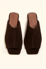 Sandalia mule de gamuza marrón, de una sola pieza con diseño asimétrico, punta cuadrada y suela plana.
