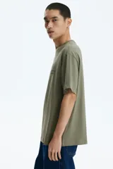 Remera de algodón verde militar con cuello redondo y estampado frontal con texto en color gris.