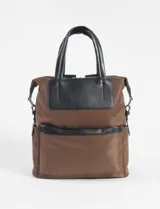 Mochila de diseño versátil en color marrón, confeccionada en tela técnica con detalles en cuero vegano negro. Cuenta con manijas superiores para llevar como bolso, correas ajustables, bolsillo frontal con cierre y compartimento principal con cierre.