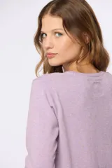 Buzo tejido en hilo de algodón color beige, con cuello redondo y manga larga. Presenta un corte clásico y un pequeño detalle metálico en la parte inferior izquierda.