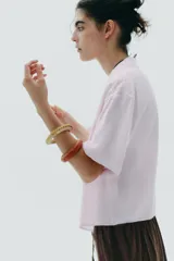 Pack de cuatro pulseras rígidas de madera recubiertas con rafia tejida en tonos rosados, naranjas y verde oliva.