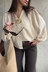 Camisa beige de manga larga con diseño abullonado y puños elastizados, escote en V con botones frontales y sutiles bordados florales tono sobre tono.