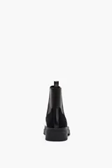 Bota Chelsea negra con paneles laterales elásticos, uno en negro y otro en gamuza negra. Detalle de cuero marrón en la parte trasera superior y suela track.