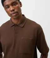 Remera polo de manga corta y corte regular, confeccionada en tejido texturizado color marrón, con cuello camisero, cartera corta con botones y un bolsillo aplicado en el pecho.