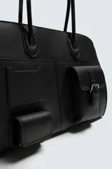 Bolso de viaje negro con acabado grabado y diseño de múltiples bolsillos frontales. Dispone de un compartimento principal con cierre magnético, un bolsillo interno con cremallera y tres bolsillos exteriores de diversos tamaños con cierre de imán. Incluye dos asas de mano superiores.