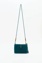 Cartera tipo bandolera de terciopelo color verde petróleo, con bordado central de estrellas en pedrería y mostacillas. Incluye una borla decorativa lateral y correa trenzada con detalles metálicos.