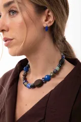 Collar corto compuesto por una variedad de cuentas que incluyen piedras naturales, cristales checos, madera y acrílico en tonos azules, marrones y verdes. Cuenta con un cierre de cadena de acero quirúrgico ajustable.