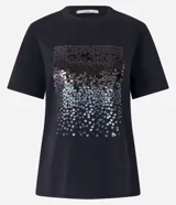 Remera negra de algodón con corte slim, cuello redondo y mangas cortas. Presenta un bloque rectangular frontal con lentejuelas plateadas.