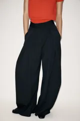 Pantalón de tiro medio con diseño wide leg, confeccionado en tejido con viscosa. Presenta un patrón de rayas diplomáticas, bolsillos laterales ocultos y detalle de pinzas pronunciadas en el delantero. Cierre frontal con cremallera, botón y ganchos metálicos.