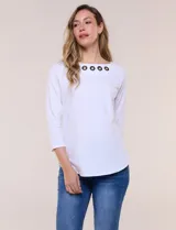 Remera blanca de algodón con elastano, de corte semi holgado, escote bote con ojalillos metálicos frontales, mangas tres cuartos raglán y ruedo asimétrico curvado.