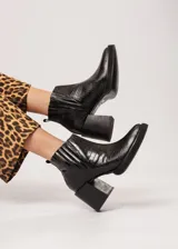 Botín negro de cuero con elástico lateral y cierre interno. Tiene plataforma delantera de 2 cm y taco de 8 cm.