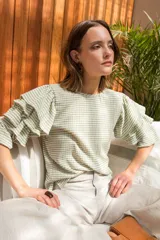 Blusa de spandex con estampado vichy en tonos pistacho y blanco, con mangas al codo adornadas con tres volados y puños elásticos. Cierre con botón en la parte posterior.