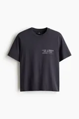 Remera de algodón color gris oscuro con cuello redondo y estampado pequeño en el pecho con texto en color blanco.
