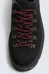 Zapato de cordones estilo trekking para hombre, confeccionado en piel con acabado de serraje color marrón. Presenta enganches metálicos para los cordones, cuello acolchado en color negro y una suela de goma con volumen y efecto moteado.