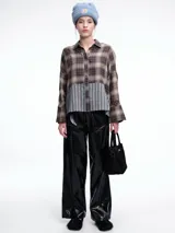 Camisa de corte relajado con diseño combinado. La parte superior presenta un estampado a cuadros en tonos marrones y negros, mientras que la parte inferior destaca por un panel de rayas verticales en color bordó. Cuenta con cierre frontal de botones y mangas largas.