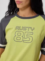 Remera bicolor Rusty con cuerpo verde lima y mangas ranglán grises con dos rayas blancas en los puños. Estampado frontal con el logo de la marca y el número 85.