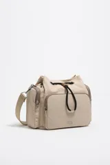 Bolso bandolera de estructura blanda en color beige, con cierre de cordón ajustable y bolsillo frontal con cierre. Incluye correa regulable de tejido y logo metálico de la marca en la parte inferior.
