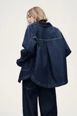 Campera camisera en denim rígido color azul, con cuello camisero, cierre frontal de botones, bolsillos de parche delanteros y bajo redondeado.