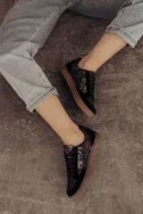 Zapatillas negras con paneles laterales de efecto piel de serpiente metalizado en tonos bronce y negro. Tienen cordones negros y suela de goma color caramelo.