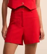 Bermuda femenina de sastrería color rojo, confeccionada en tejido de crepé. Presenta trabillas en la cintura, cierre delantero y bolsillos falsos.