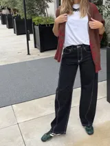 Pantalón de jean de corte recto y tiro medio, con un acabado de teñido ácido en tonos oscuros. Presenta bolsillos traseros con bordados decorativos en color negro y una etiqueta de cuero en la cintura.