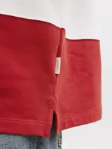 Buzo tipo polo de manga larga con diseño de franjas horizontales anchas en color rojo y blanco, cuello camisero blanco y cierre frontal parcial con solapa y botones ocultos.