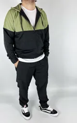 Campera deportiva combinada verde y negra de nylon, con capucha, cierre frontal y logo bordado en el pecho.