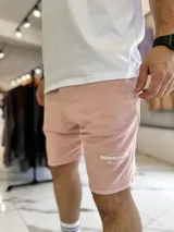 Bermuda de jogging color beige, con bolsillos laterales y estampa con texto blanco en la pierna izquierda.