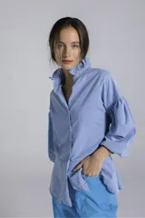 Camisa de manga larga abullonada con cuello mao y detalle de volados. Presenta un corte peplum y cierre frontal con botones.