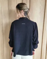 Blusa celeste de algodón con estampado de rayas verticales formadas por pequeños motivos blancos, escote en V con cuello alto fruncido y mangas largas abullonadas con puños amplios.