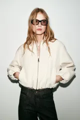Chaqueta de corte corto y diseño abullonado en color marrón oscuro, con cuello solapa, mangas largas con puños elásticos y cierre frontal con cremallera metálica. Cuenta con bolsillos delanteros de doble vivo.