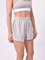 Short deportivo de color gris claro con cintura elástica fruncida y cordón ajustable blanco. Presenta bandas laterales en color verde militar y ribetes blancos en los bordes curvos de las piernas.