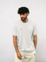 Remera de algodón gris claro con cuello redondo y mangas cortas. Presenta un estampado circular pequeño en el pecho con el logo de Umbro y la frase 'Born to play'.