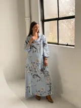 Vestido largo celeste con estampado floral en tonos blancos y grises, de corte holgado, mangas largas y cuello drapeado.