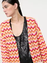 Saco tejido largo con diseño de ondas en tonos naranja, rosa, amarillo y blanco. Tiene bolsillos delanteros y mangas largas acampanadas.
