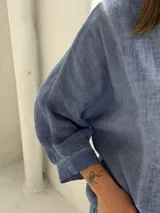 Camisa azul de lino con cuello mao, cierre frontal con botones y mangas largas abullonadas con puños elásticos.