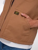 Chaleco de trabajo Caterpillar, color marrón, con cierre frontal, cuello tipo bomber y bolsillos laterales. Presenta parche de la marca en el pecho y forro interno.