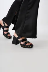 Sandalias de cuero negro con plataforma y taco cuadrado, tiras anchas sobre el empeine y detalle de tachas doradas en la base.