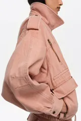 Chaqueta de corte globo color salmón, confeccionada en algodón lavado. Presenta cierre frontal con cremallera, cuello con solapas grandes, mangas largas con puños ajustables, bolsillos laterales y calce holgado.