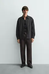 Sobrecamisa de corte relajado confeccionada en denim de algodón con diseño a rayas verticales. Presenta cuello solapa, cierre frontal de botones, manga larga con puños abotonados y un bolsillo plastrón en el pecho.