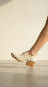 Zapato tipo slip-on color beige, confeccionado en cuero natural con combinación de texturas lisas y grabadas. Presenta un taco cuadrado de madera y una suela dentada de goma.