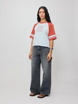 Remera bicolor Rusty con cuerpo verde lima y mangas ranglán grises con dos rayas blancas en los puños. Estampado frontal con el logo de la marca y el número 85.