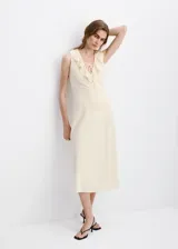 Vestido midi recto color beige sin mangas, con cuello en V con solapa de volantes bordados y cordones entrecruzados en el escote.