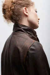 Blazer de cuero marrón con cierre frontal, cuello alto, múltiples bolsillos con hebillas y detalle de triángulo de cuero en el pecho.