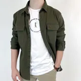 Sobrecamisa verde militar de gabardina con cuello clásico, cierre frontal abotonado, mangas largas con puños abotonados y dos bolsillos de parche en el pecho.