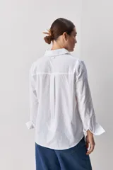 Camisa de algodón blanca, de calce relajado, con cuello clásico, mangas largas y cierre frontal con botones.