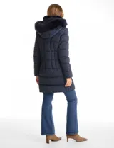 Campera puffer larga de color azul marino con capucha desmontable con borde de piel sintética. Cuenta con cierre frontal metálico dorado con logo grabado y bolsillos laterales con cierre.