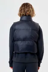 Chaleco puffer acolchado Topper de corte cropped, color negro, con cuello alto, cierre frontal y logo de la marca en el pecho.