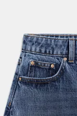 Jeans de tiro alto con diseño barrel, confeccionados en denim azul. Presentan cinco bolsillos, cierre frontal con botones y detalle de costuras verticales en el frente y la espalda. Su corte es holgado en la pernera y se estrecha hacia el tobillo.