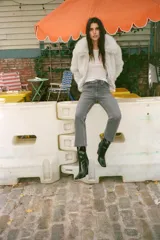 Jeans de tiro alto color marrón oscuro con acabado lavado, corte recto/flare y bajo cropped sin costuras. Presenta cinco bolsillos y cierre frontal con cremallera y botón metálico.